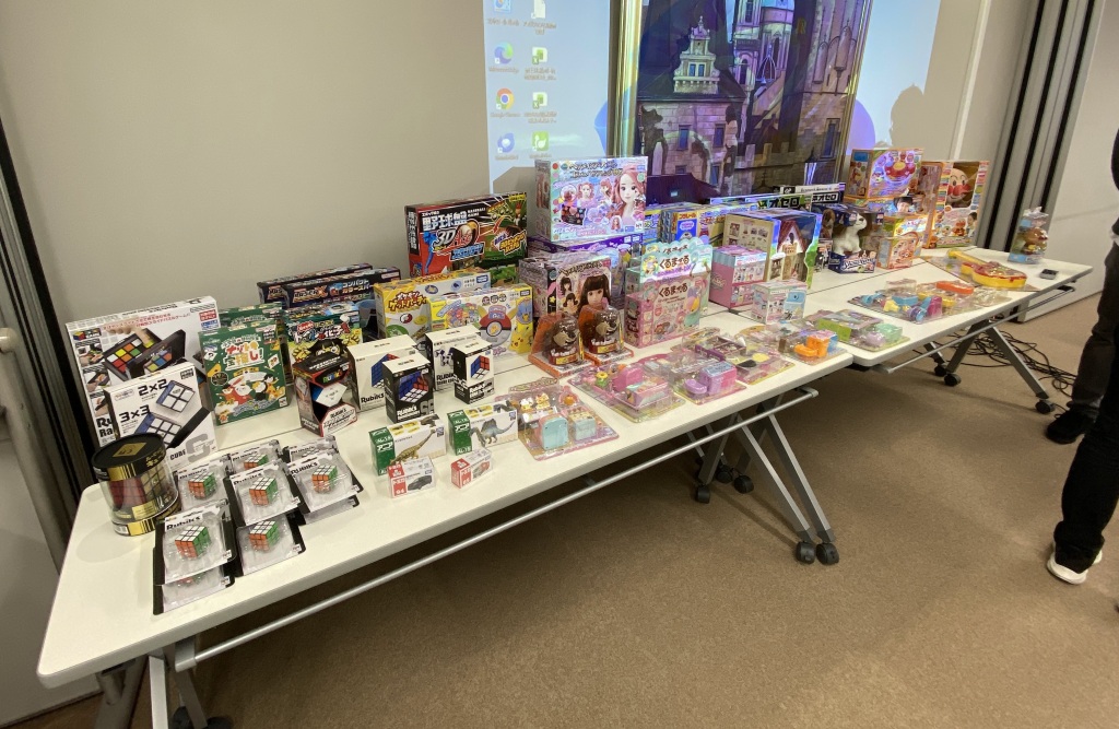 会議室のテーブルの上に40個ほどのおもちゃが並べてある写真
